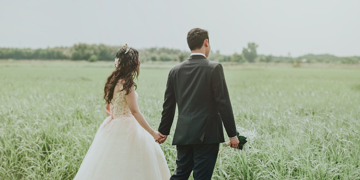 Bride and groom walking hand in hand through a field